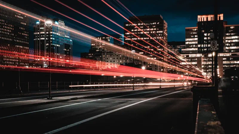 Long exposure photo of city traffic at night creating red light trails across urban buildings