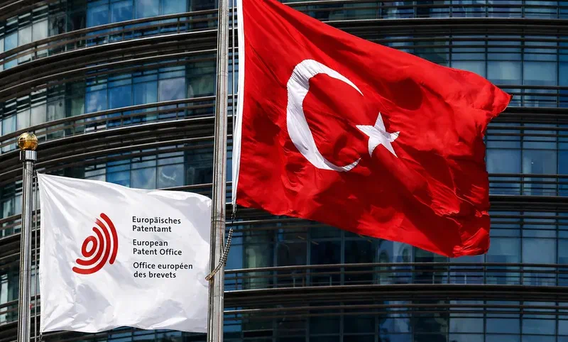 Turkish flag alongside European Patent Office (EPO) flag on white background in front of modern building