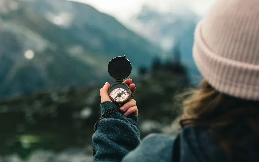 Person holding a compass while looking at a mountain landscape symbolizing direction and guidance
