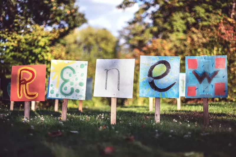Colorful hand-painted letters spelling “renew” displayed outdoors on small wooden signs