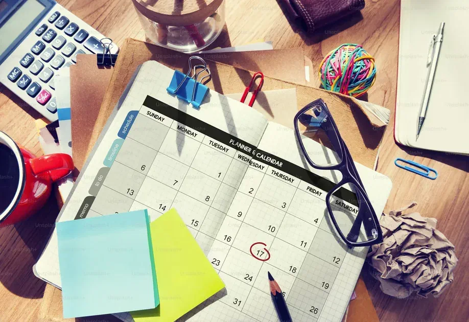 Monthly planner calendar with a marked deadline on a cluttered office desk with stationery and glasses