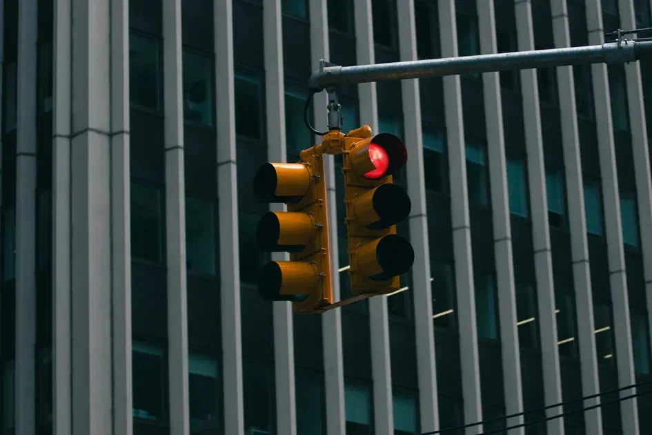 Red traffic light suspended above an urban intersection with a modern office building in the background.