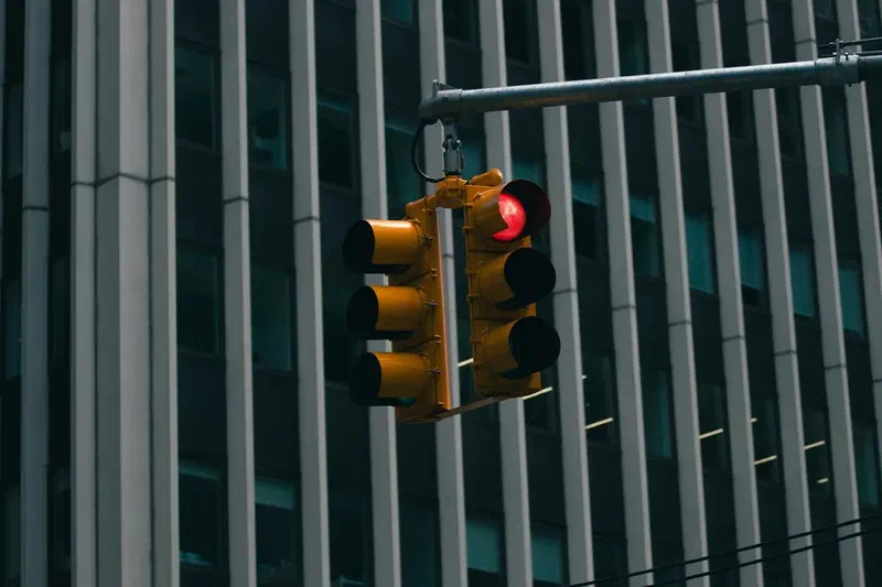 Red traffic light suspended above an urban intersection with a modern office building in the background.