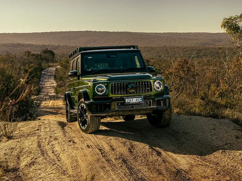 Green off-road SUV driving on a rugged dirt road in a remote natural landscape