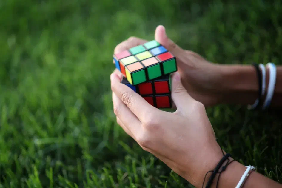 Close-up of hands solving a colorful Rubik’s cube on grass background